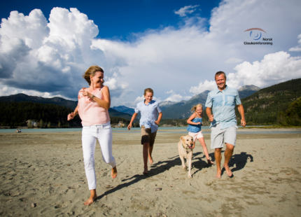 bilde av en familie som løper på strand med fjell i bakgrunnen.